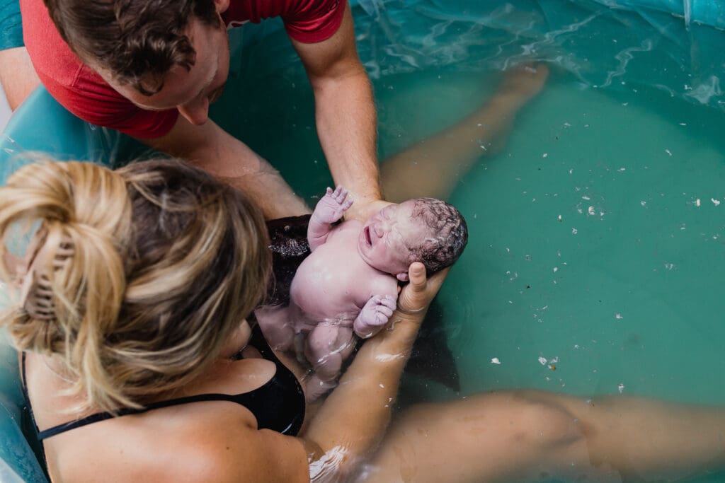 Mom holding newborn baby in birthing tub at home birth
