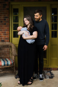 Mom and dad holding newborn daughter on front porch