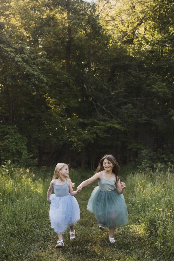 Sisters running through grassy meadow during spring family photos