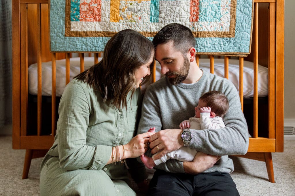 Mom and dad sitting on floor in front of crib in baby's nursery
