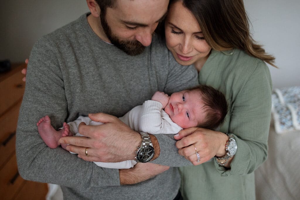 Mom and dad holding newborn baby boy in bedroom
