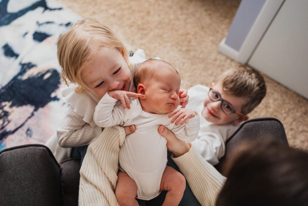 Older siblings looking at baby sister in mom's lap