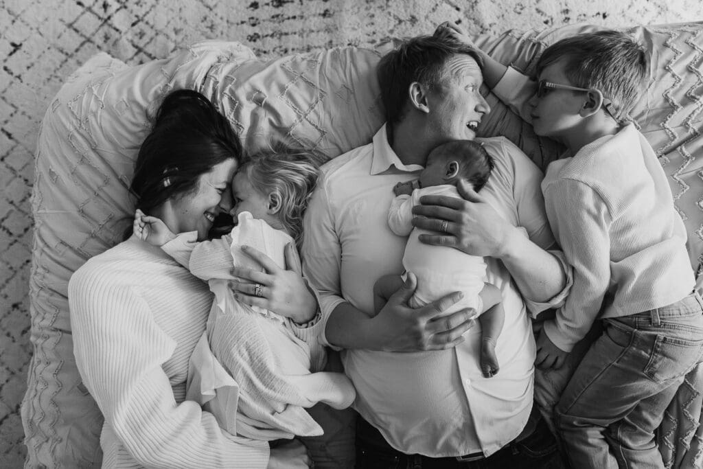 Family of five on bed snuggling with newborn baby sister