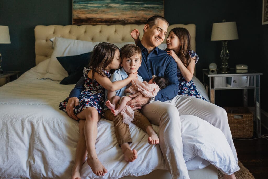 Siblings and newborn baby girl on bed with dad during Cleveland newborn photography session

