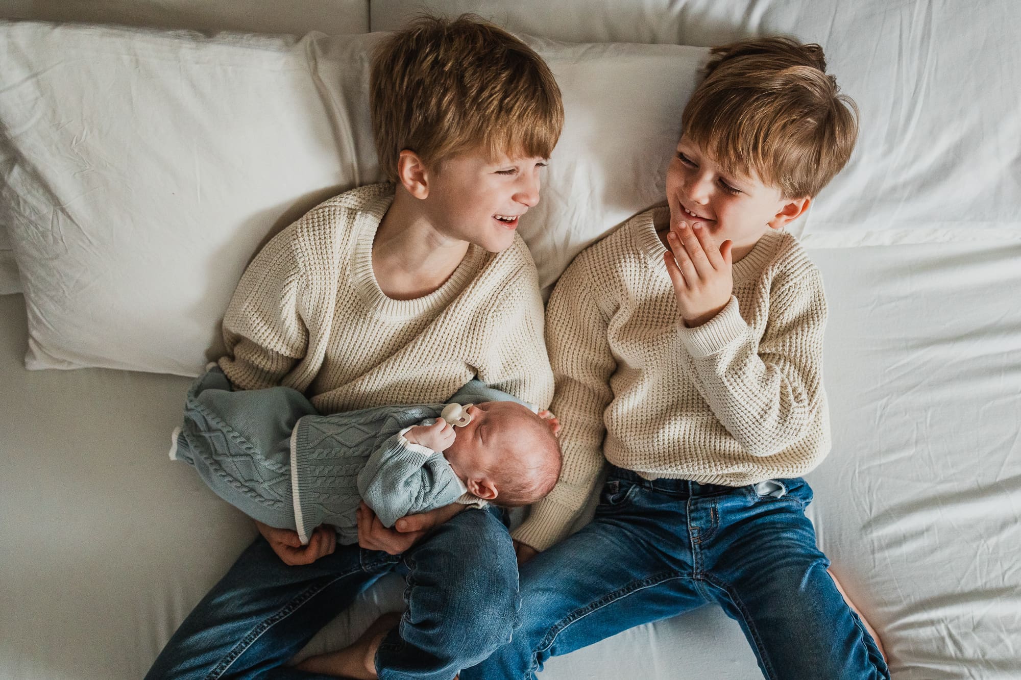 Two big brothers holding newborn baby brother on bed during Cleveland newborn photography session