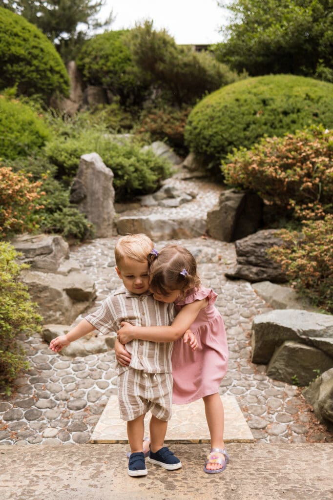 Brother and sister hugging on rocks at family photo session at Cleveland Botanical Garden
