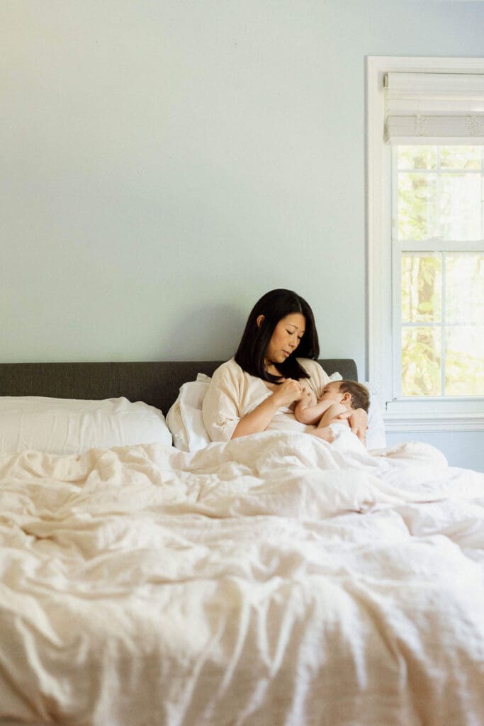 Mother nursing baby on white bed during in-home family session. 