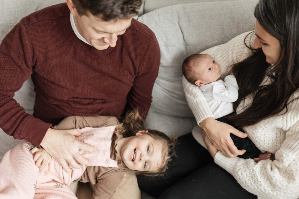Mom holding newborn and dad tickling toddler during lifestyle photography sessions.