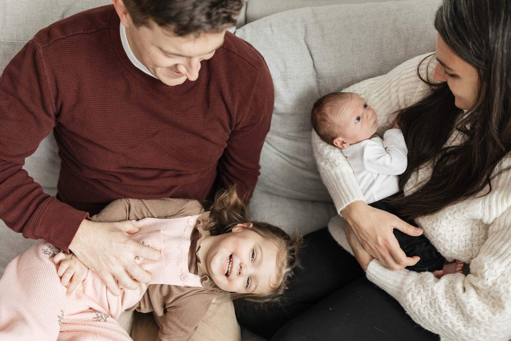 Mom holding newborn and dad tickling toddler on couch during in-home lifestyle photography session in Cleveland, OH.