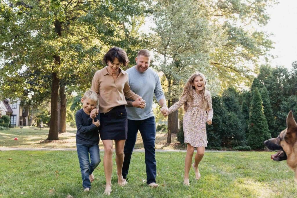 Family of four running through their front yard laughing during lifestyle photography session in Cleveland, OH.