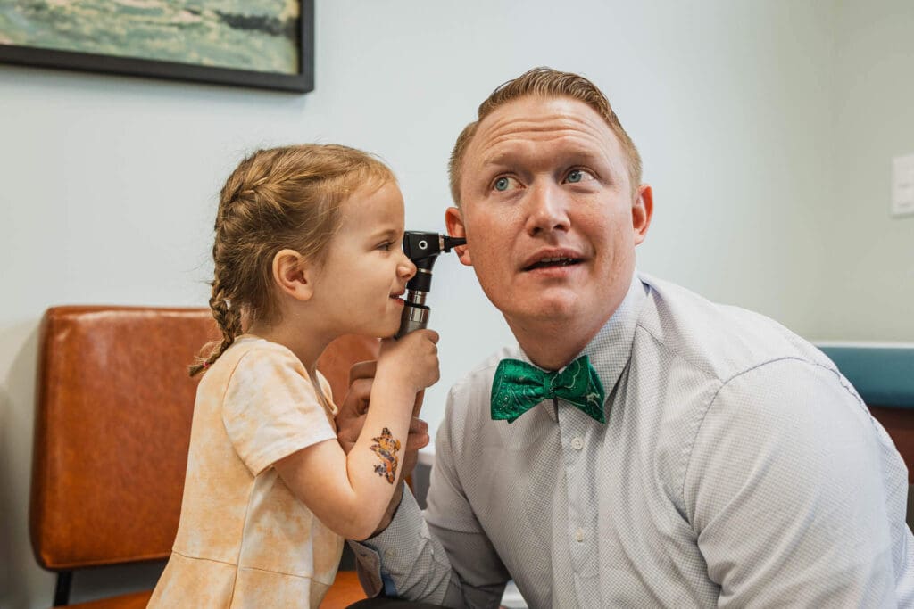 A young girl playfully uses an otoscope to check a pediatrician’s ear at Zest Pediatrics in Cleveland, OH, highlighting the clinic’s child-friendly approach.