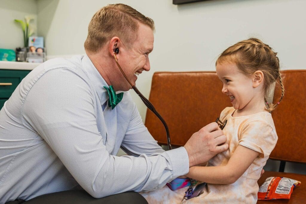 Dr. Mike Perisa, a pediatrician at Zest Pediatrics in Cleveland, OH, using a stethoscope to check a young patient, creating a fun and caring experience.