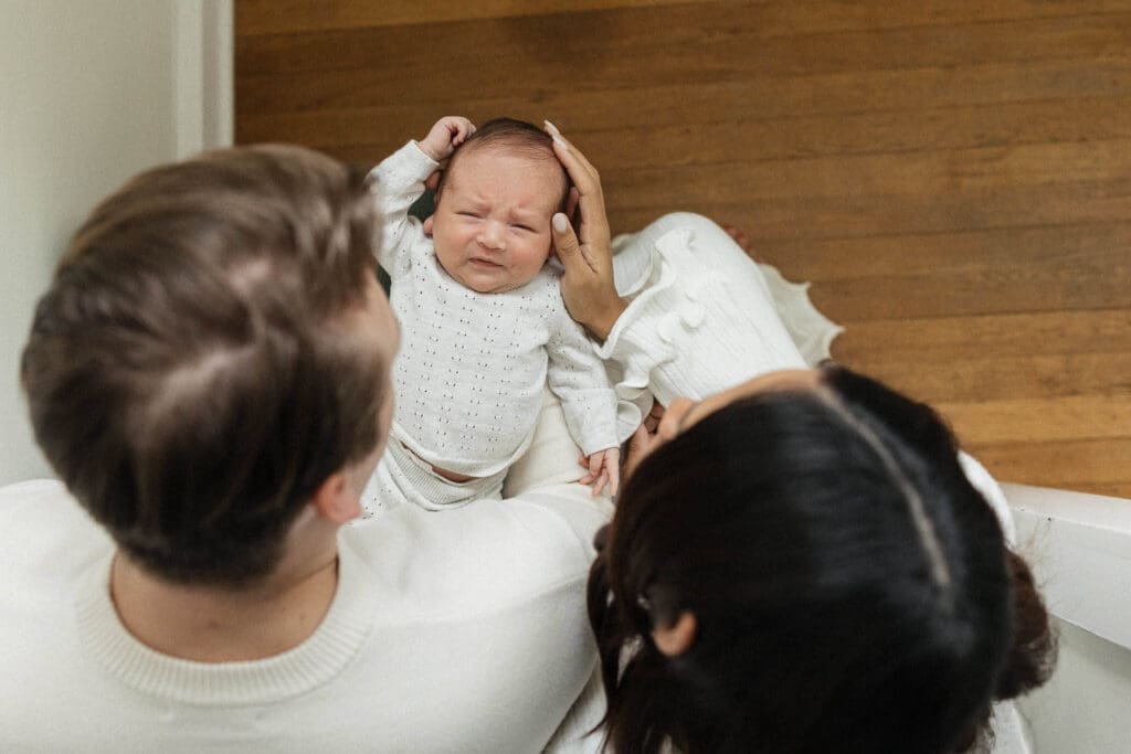 Parents gently cradle their newborn at the top of the stairs during an in-home lifestyle session—capturing the early emotions of the newborn stage.