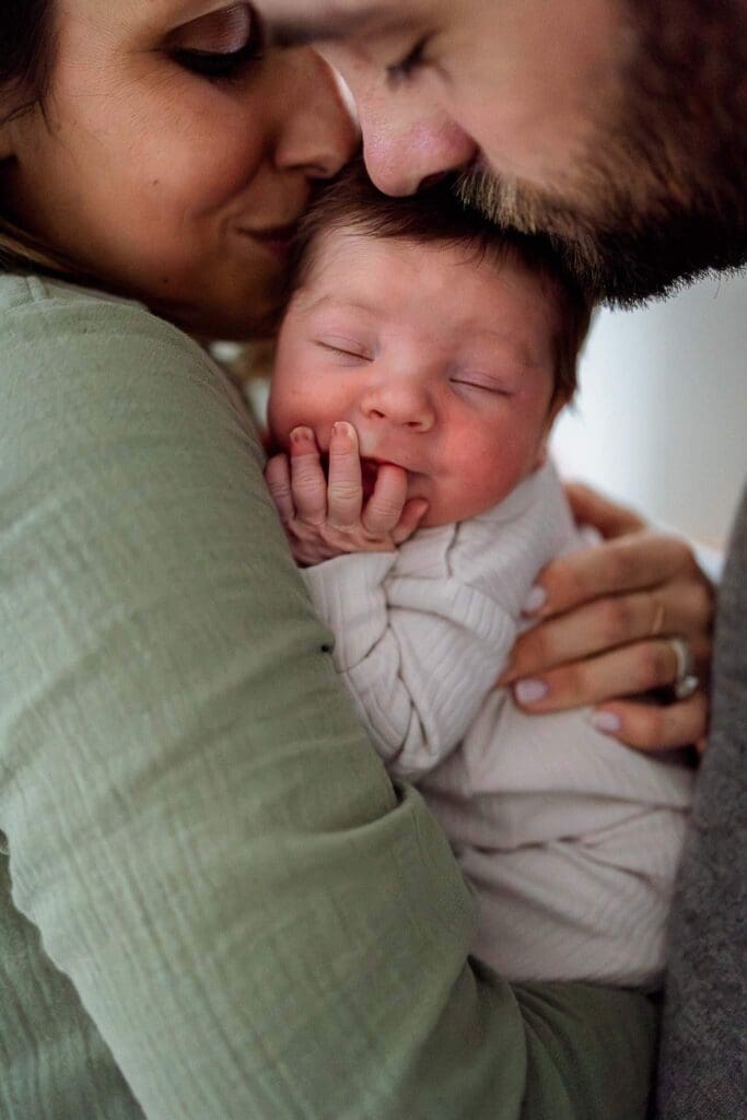 Parents snuggle and kiss their sleepy newborn—capturing connection, comfort, and the fleeting magic of the newborn stage.