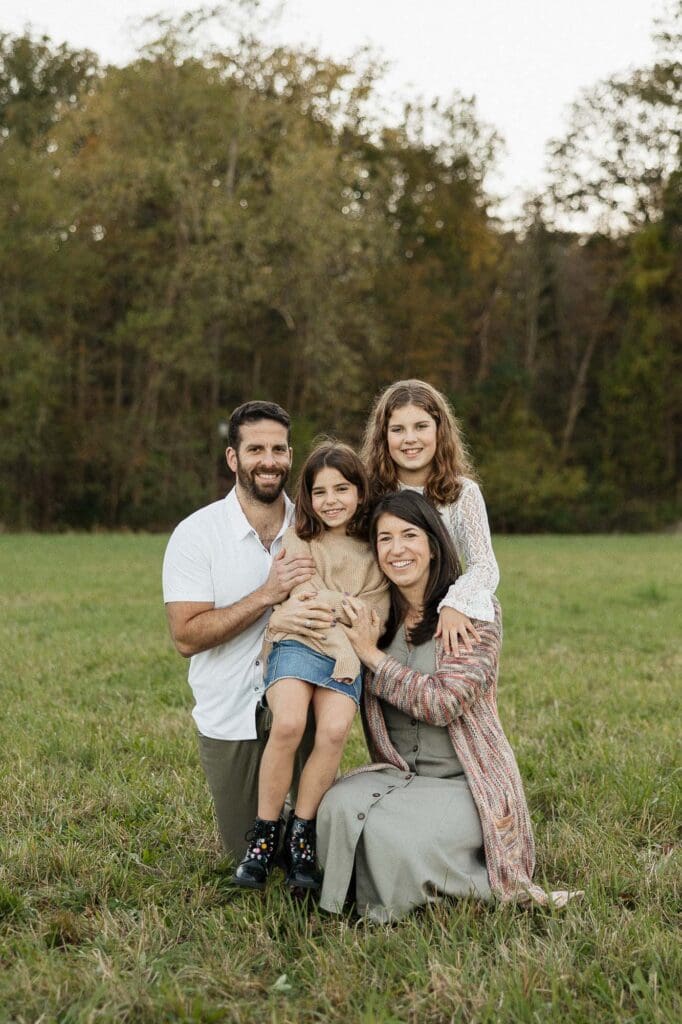 Family of four hugging with fall foliage in the background.